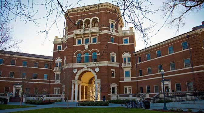 Historic red brick Oregon State University building with arched entrance and multiple windows, surrounded by leafless trees under a clear sky.