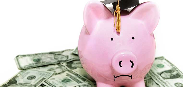 A pink piggy bank wearing a graduation cap is placed on top of scattered dollar bills, symbolizing the financial burden faced by students attending some of the most expensive out-of-state public universities.