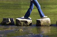 Person crossing stepping stones representing steps to finding the most merit scholarships