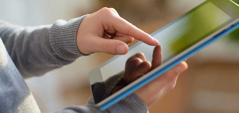 A person's hand is tapping on the screen of a tablet device, meticulously creating a college list.