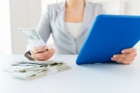 Woman with money looking at computer for college merit aid