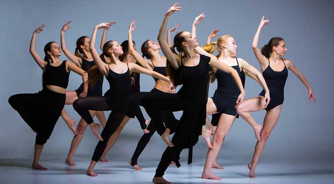 A group of Visual and Performing Arts majors in black leotards performing a synchronized contemporary dance routine in a studio setting.