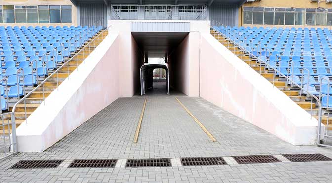 Entrance to a sports stadium with blue seating visible to the sides and a ramp leading to a tunnel under the stands, often frequented by recipients of athletic scholarships.